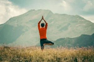 Ein junger Mann führt die Yoga Asana Berg auf einer Bergwiese in der Natur durch